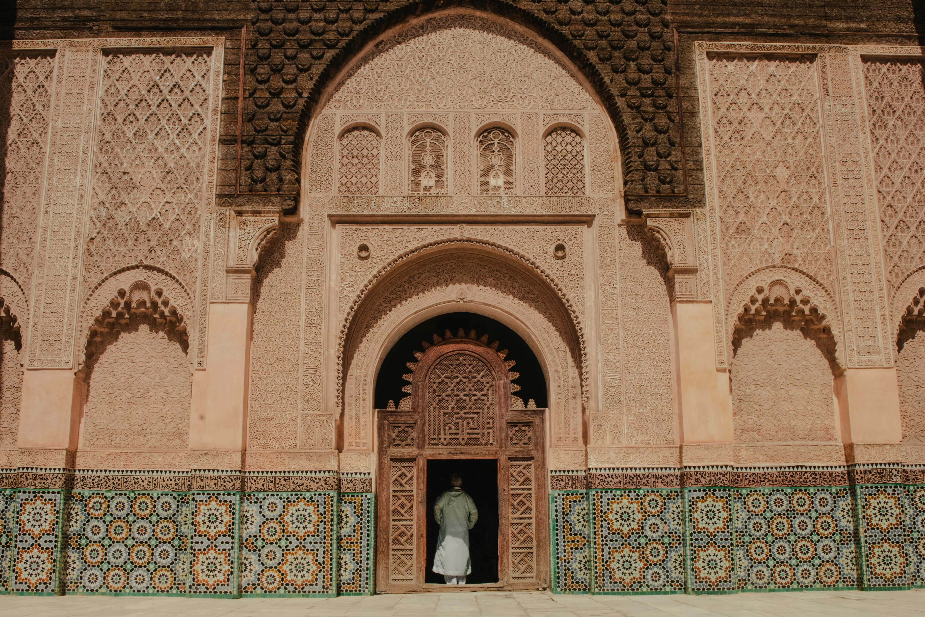 Porte sculptée de la médersa Ben Youssef à Marrakech, stuc et zellige, un visiteur sur le seuil