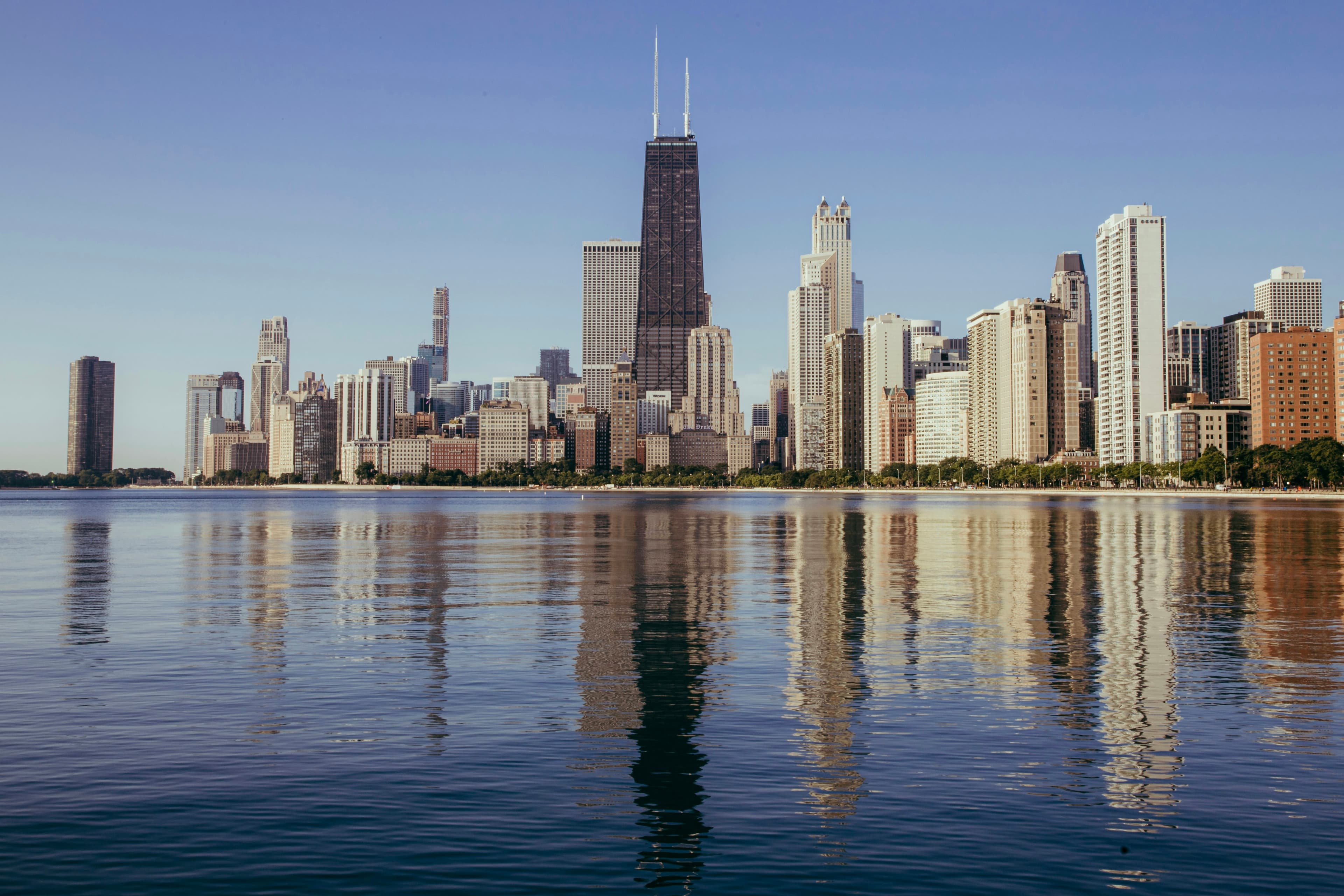 Chicago skyline reflected in calm Lake Michigan under a clear blue sky