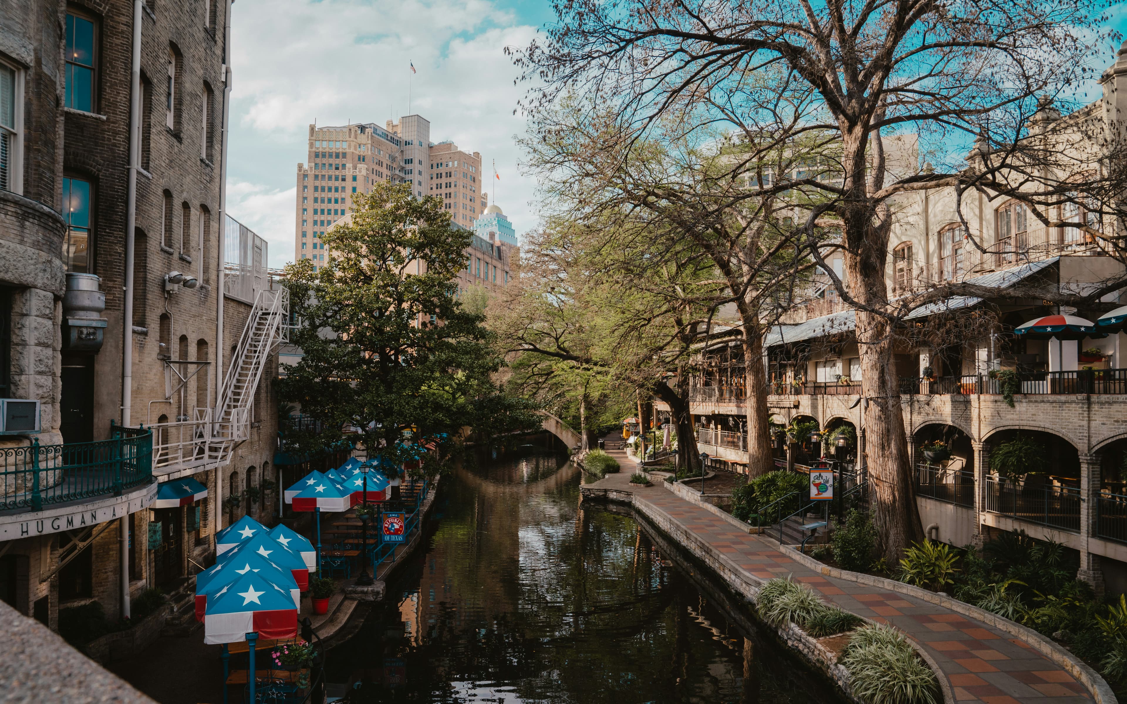 San Antonio River Walk lined with trees, cafes and stone paths on a sunny day