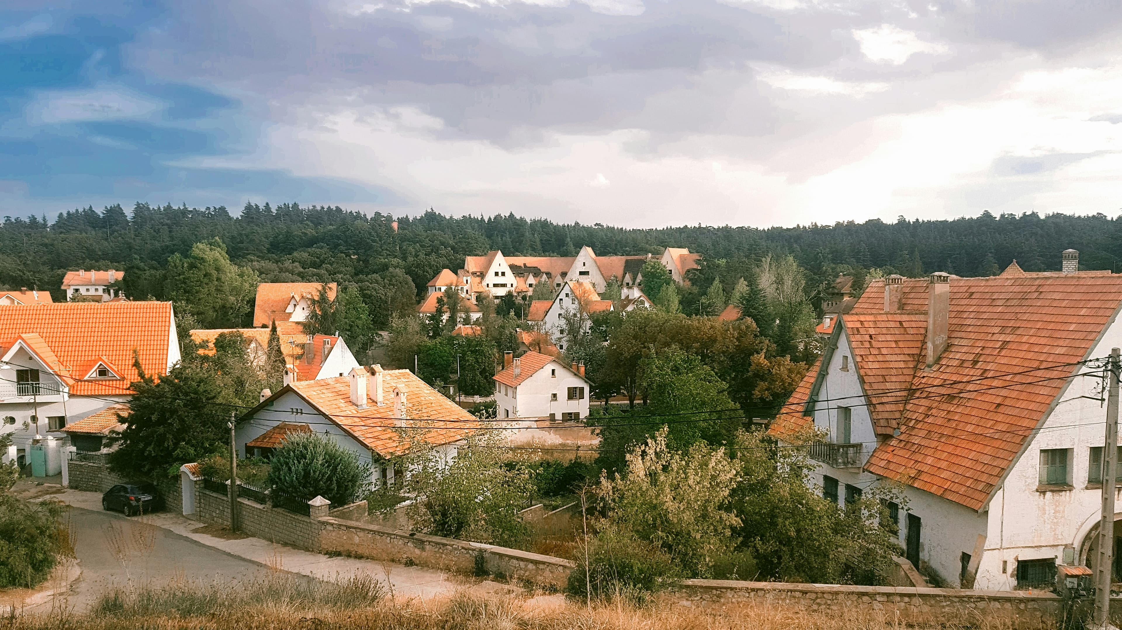 Maison au toit pentu entourée d'arbres verts sous un ciel nuageux, à Ifrane