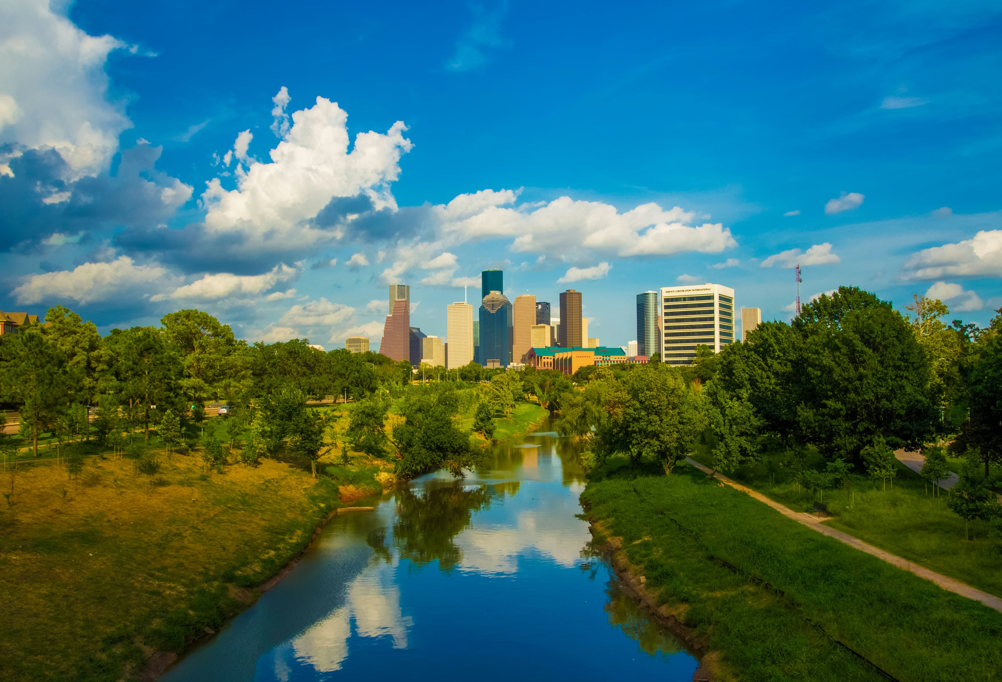 Houston skyline rising above Buffalo Bayou and green parkland on a sunny day