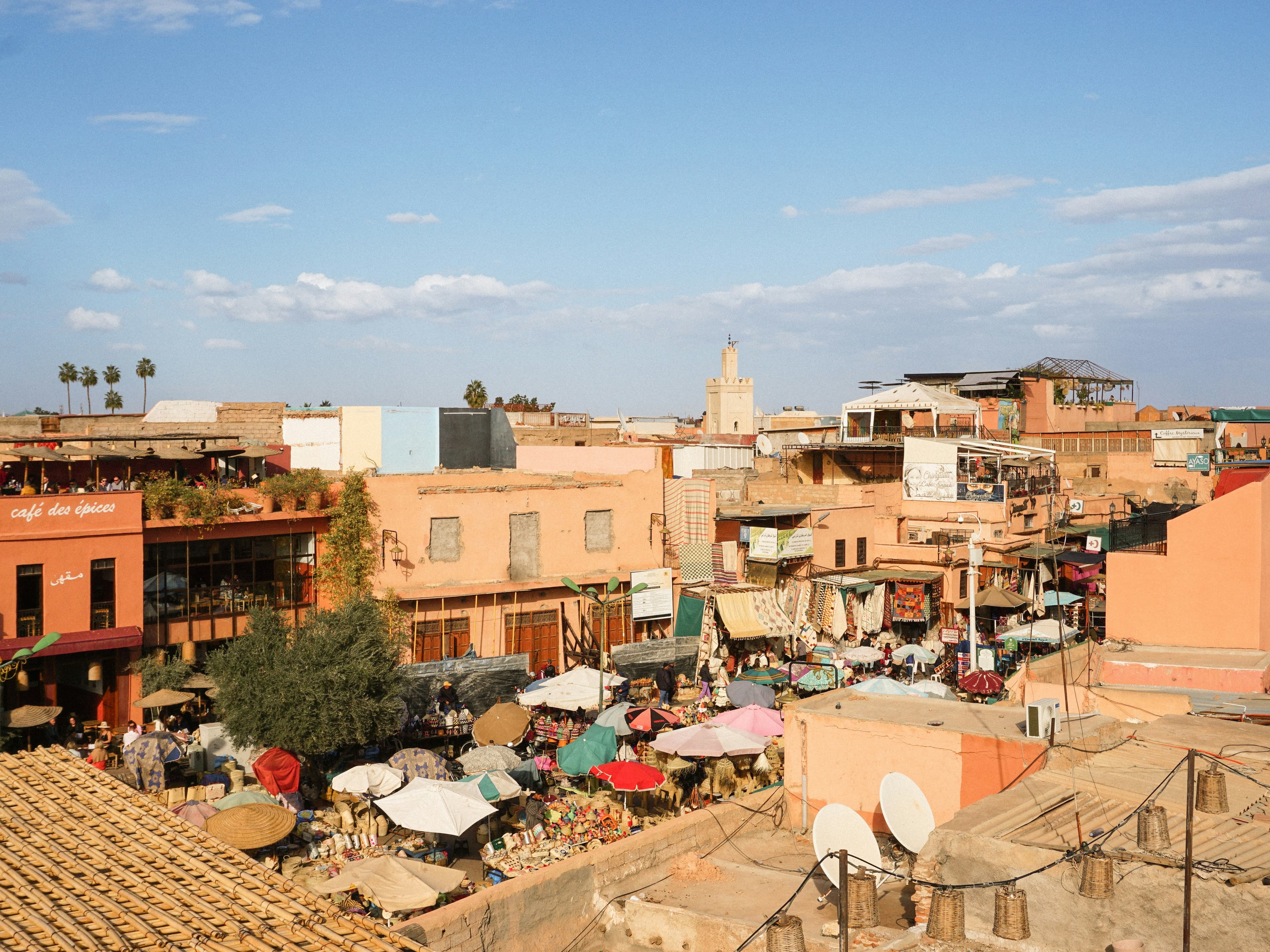 Les terrasses de la place des Épices à Marrakech, parasols du marché et minaret au loin