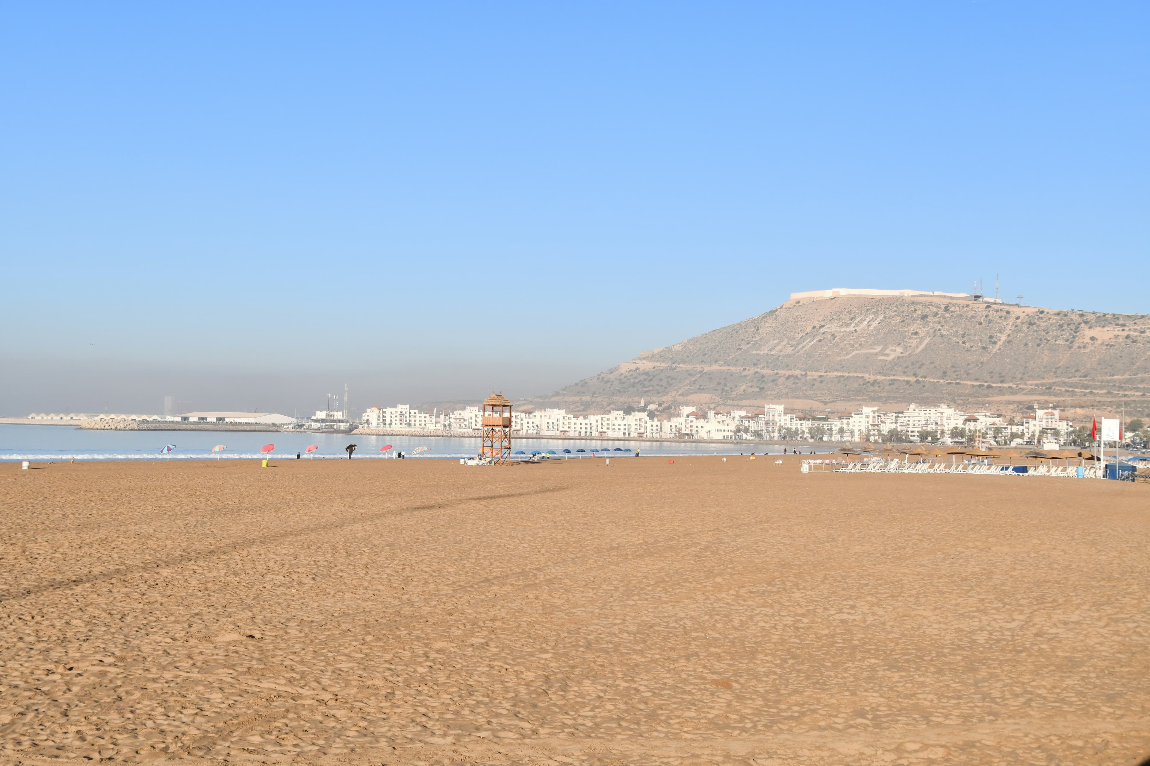 La plage d'Agadir au matin, sable et poste de surveillance, la colline de la kasbah à l'horizon