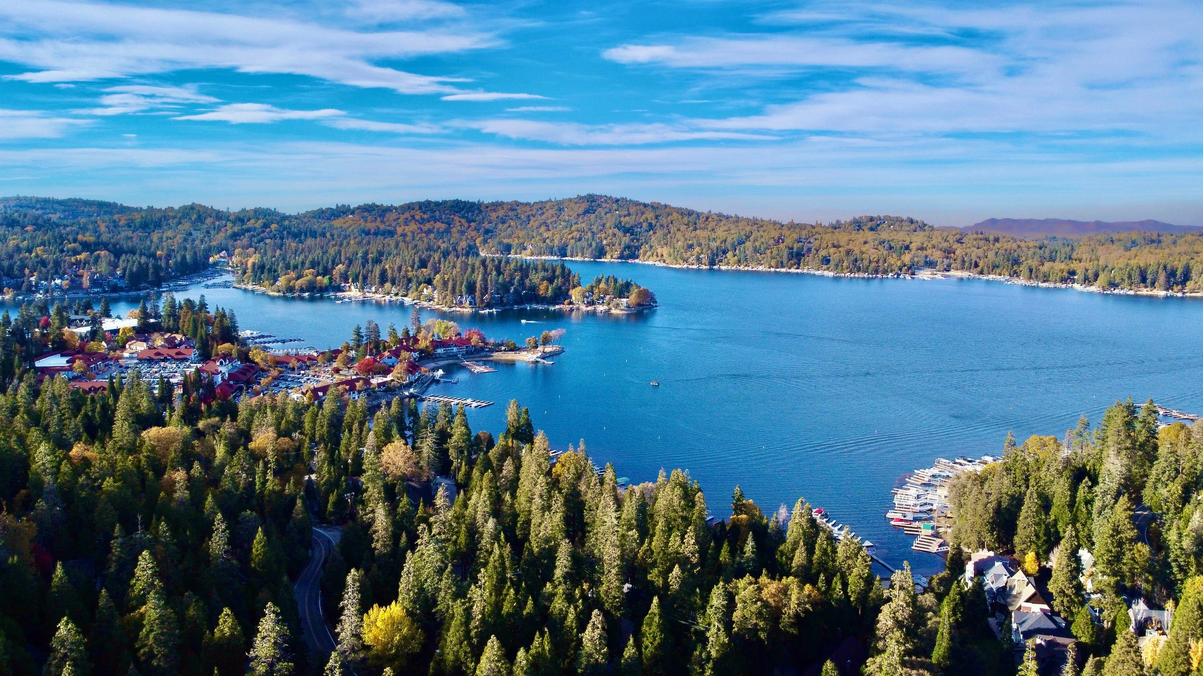 Aerial view of Lake Arrowhead surrounded by pine forest under a blue sky