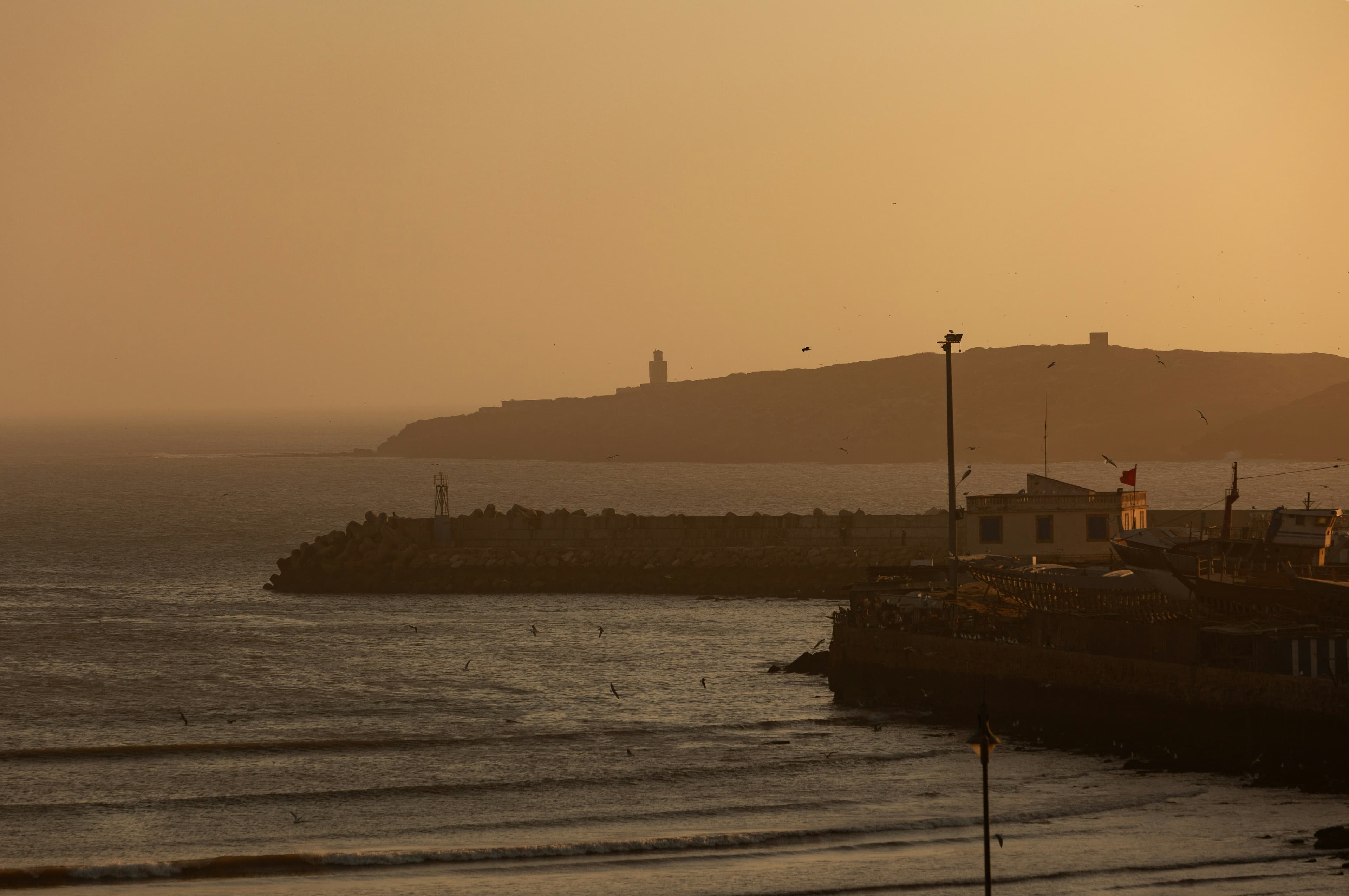 Une côte plate au coucher du soleil, un phare au loin